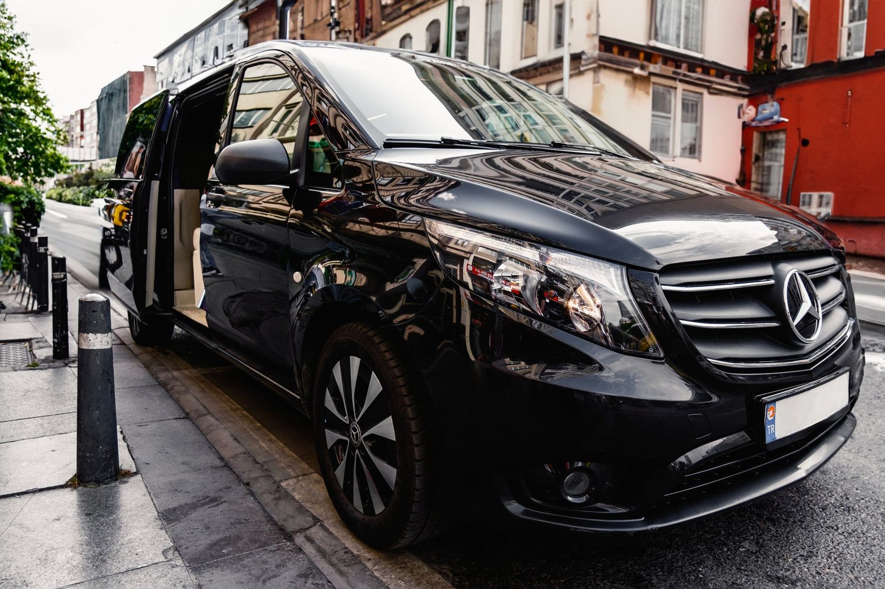 Black Mercedes-Benz V-Class chauffeur van waiting with its door open on a city street